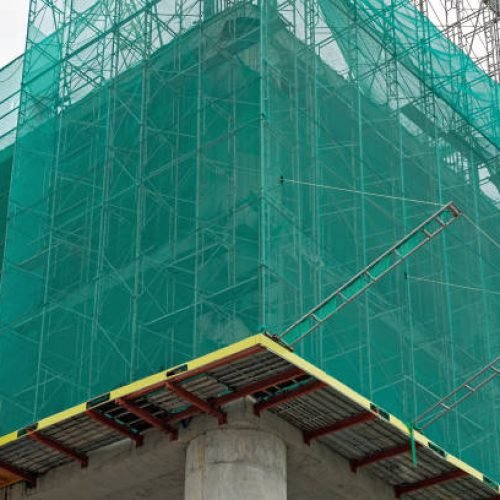 Building under construction wrapped green protection safety net.